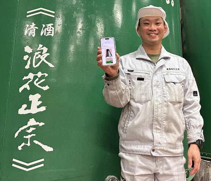 酒蔵の職人がスマートフォンを持って笑顔で立つ様子
